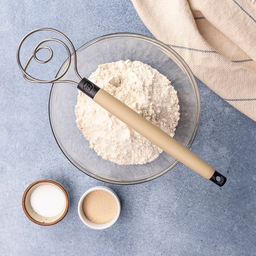 Dough whisk resting on top of a bowl containing flour and other ingredients.