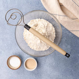 Dough whisk resting on top of a bowl containing flour and other ingredients.